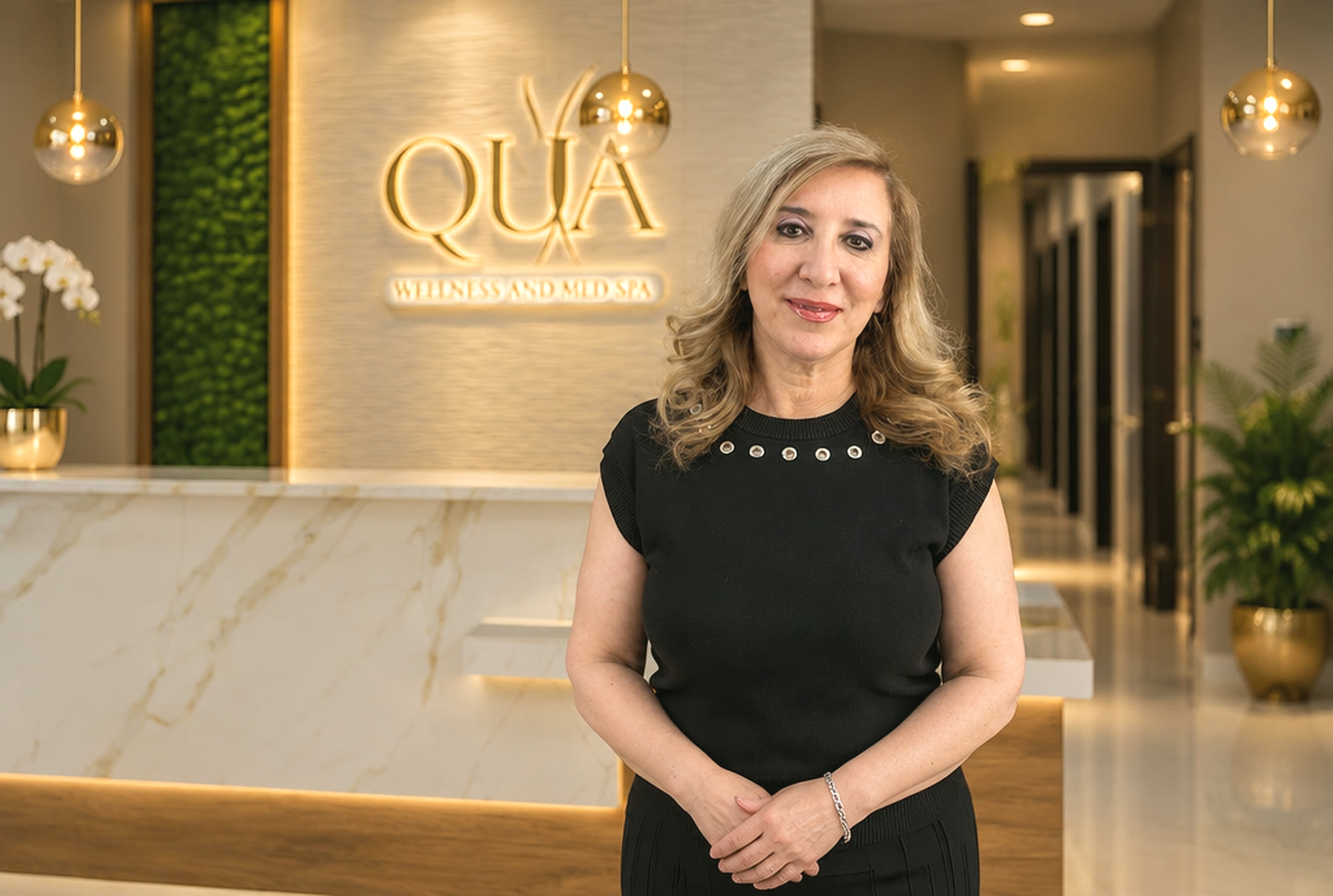 Dr. Maha Abboud at the Qua Wellness and Med Spa reception in Burr Ridge, in front of the gold Qua sign